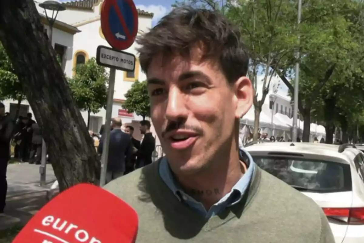 Luitingo, smiling, is interviewed on the street, with a red microphone in the foreground and a traffic sign behind him. Luitingo, smiling, is interviewed on the street, with a red microphone in the foreground and a traffic sign behind him.