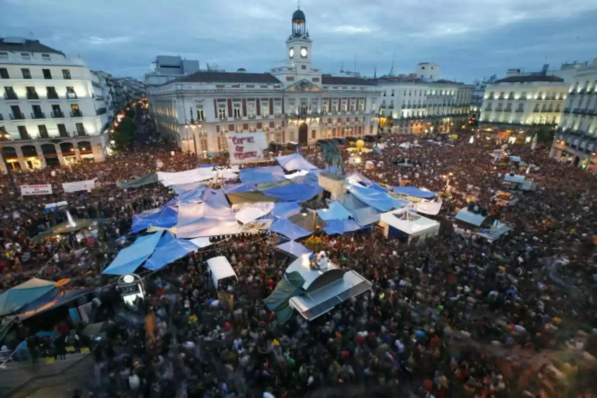 Una multitud de persones es reuneixen en una plaça pública amb tendes de campanya i pancartes.