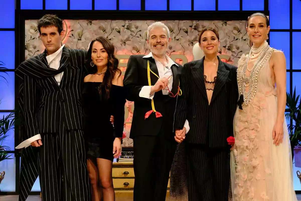 Palomo Spain, María Escoté, Lorenzo Caprile, Adriana Ugarte y Raquel Sánchez Silva posando juntas en un escenario con fondo floral y luces azules, algunas visten trajes elegantes y otras ropa formal en Maestros de la Costura.