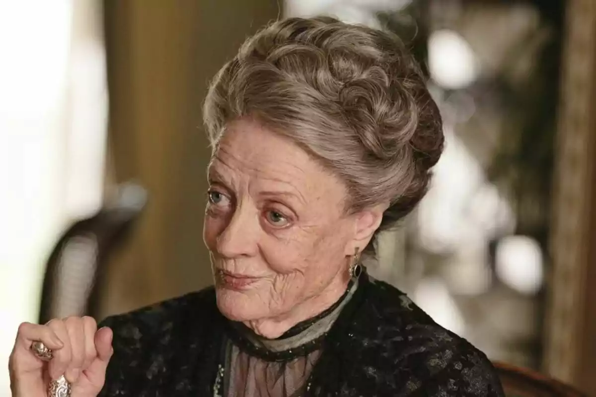 Maggie Smith amb els cabells canosos recollits i expressió pensativa, vestida amb roba elegant i fosca.