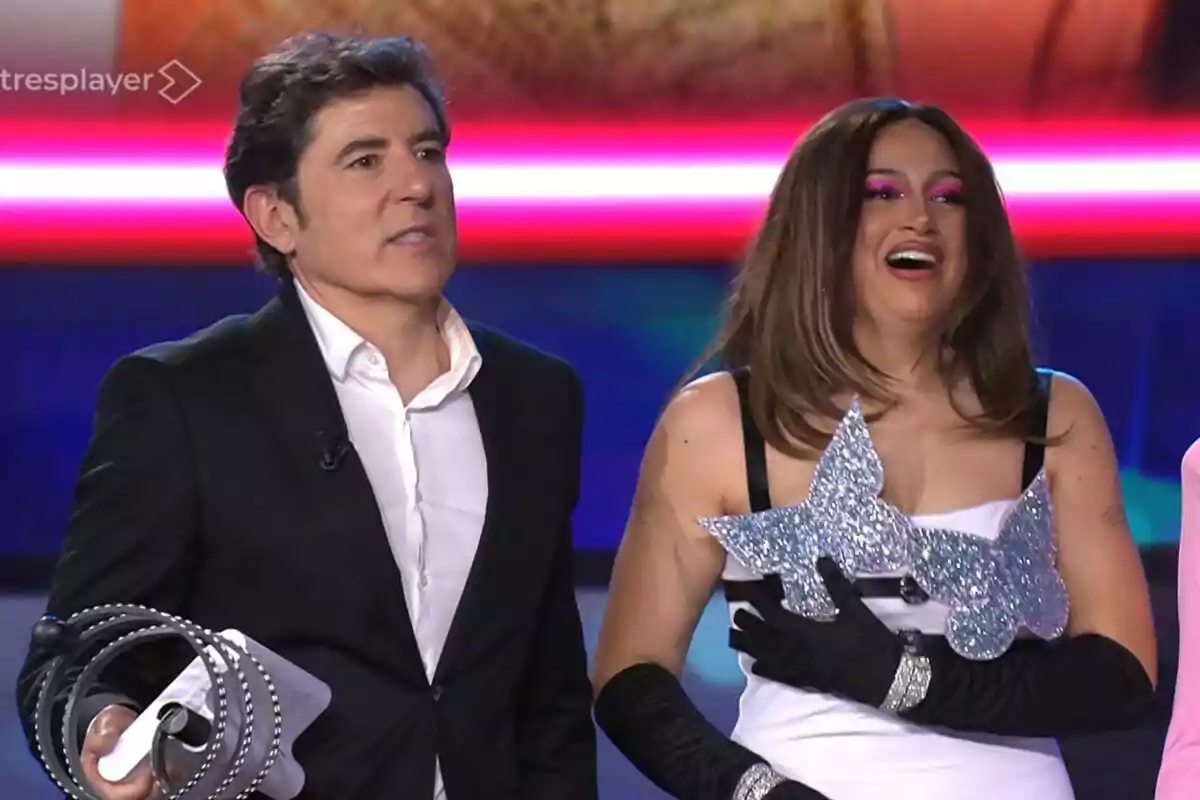 Manel Fuentes i Esperansa Grasia en un escenari, una d'elles sosté un objecte brillant en forma de papallona mentre somriu, i l'altra porta un vestit formal fosc a Tu Cara Me Suena. Manel Fuentes i Esperansa Grasia en un escenari, una d'elles sosté un objecte brillant en forma de papallona mentre somriu, i l'altra porta un vestit formal fosc a Tu Cara Me Suena.
