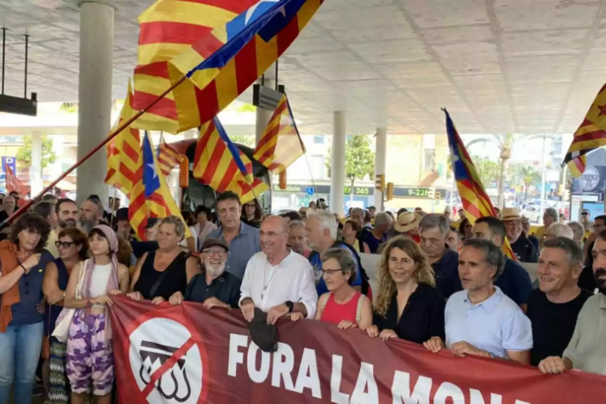 L'ANC sosté una pancarta que diu "FORA LA MONARQUIA" mentre onegen banderes amb franges vermelles i grogues en una manifestació.