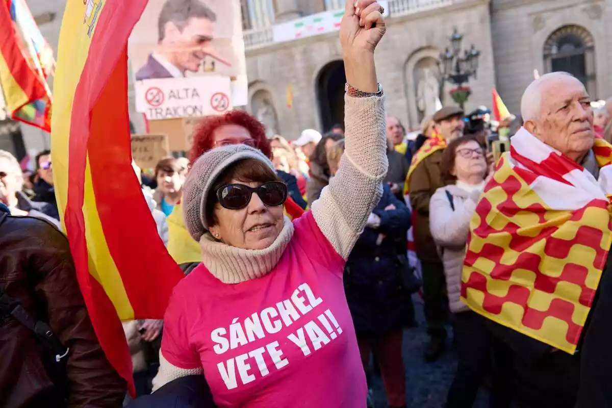 Manifestació constitucionalista amb una dona en primer pla amb una samarreta rosa i el lema 'Sánchez vete ya'. De fons, diversos manifestants amb banderes espanyoles i de Tabarnia i una foto de Pedro Sánchez amb el nas allargat i la frase 'alta traïció'