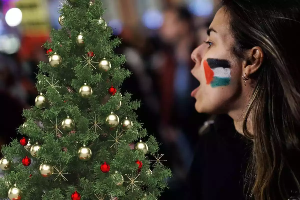 Muntatge amb una manifestant pro Palestina amb un arbre de Nadal al costat