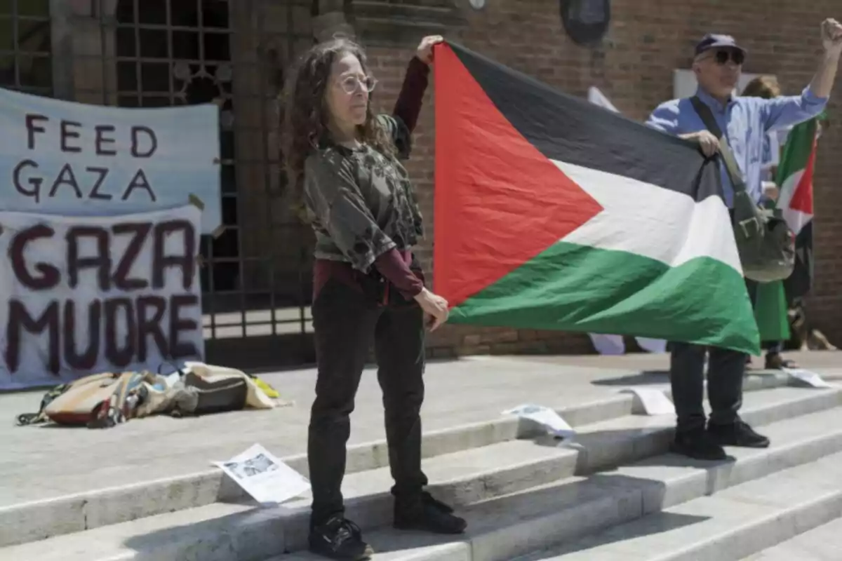 Dona sostenint una bandera de Palestina durant una manifestació, amb pancartes de suport a Gaza al fons Dona sostenint una bandera de Palestina durant una manifestació, amb pancartes de suport a Gaza al fons