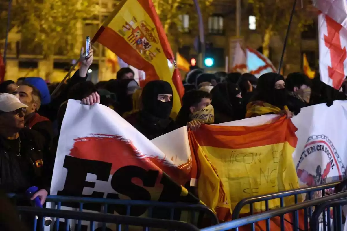 manifestants contra l'amnistia amb la cara tapada subjecten pancartes amb la bandera espanyola