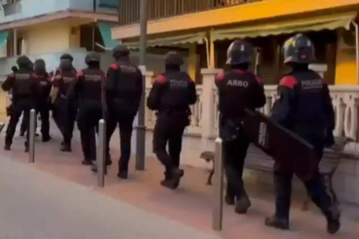 Diversos agents de policia antidisturbis caminen en fila per una vorera al costat d’un edifici de color groc.