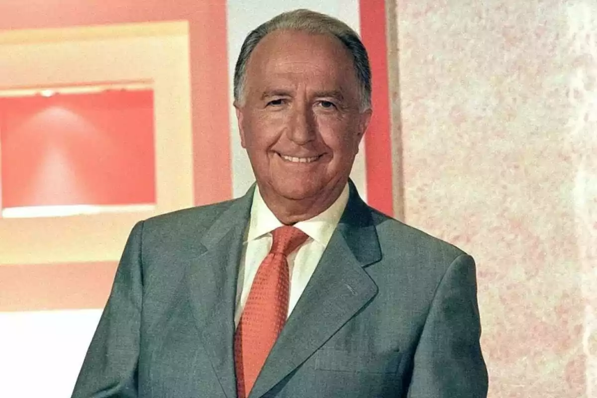 Manuel Torreiglesias gran amb vestit gris i corbata taronja somriu davant d'un fons amb tons rosats i blancs. Manuel Torreiglesias gran amb vestit gris i corbata taronja somriu davant d'un fons amb tons rosats i blancs.