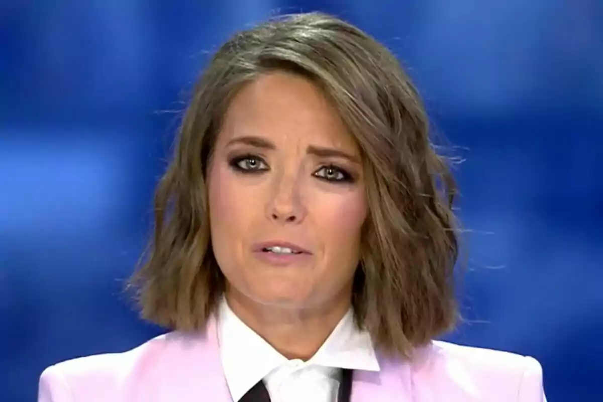 María Casado con cabello corto y castaño claro lleva un traje rosa y camisa blanca con fondo azul en Informativos Telecinco.