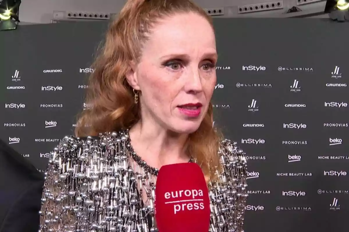 María Castro in a shiny dress being interviewed by Europa Press at an event with a background of brand logos. María Castro in a shiny dress being interviewed by Europa Press at an event with a background of brand logos.