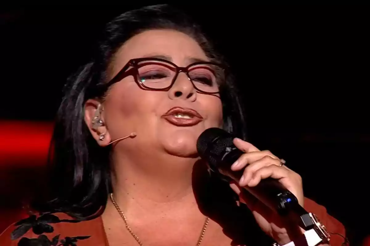 Captura de María del Monte con gafas y un micrófono canta en un escenario iluminado en el escenario de Dúos Increíbles