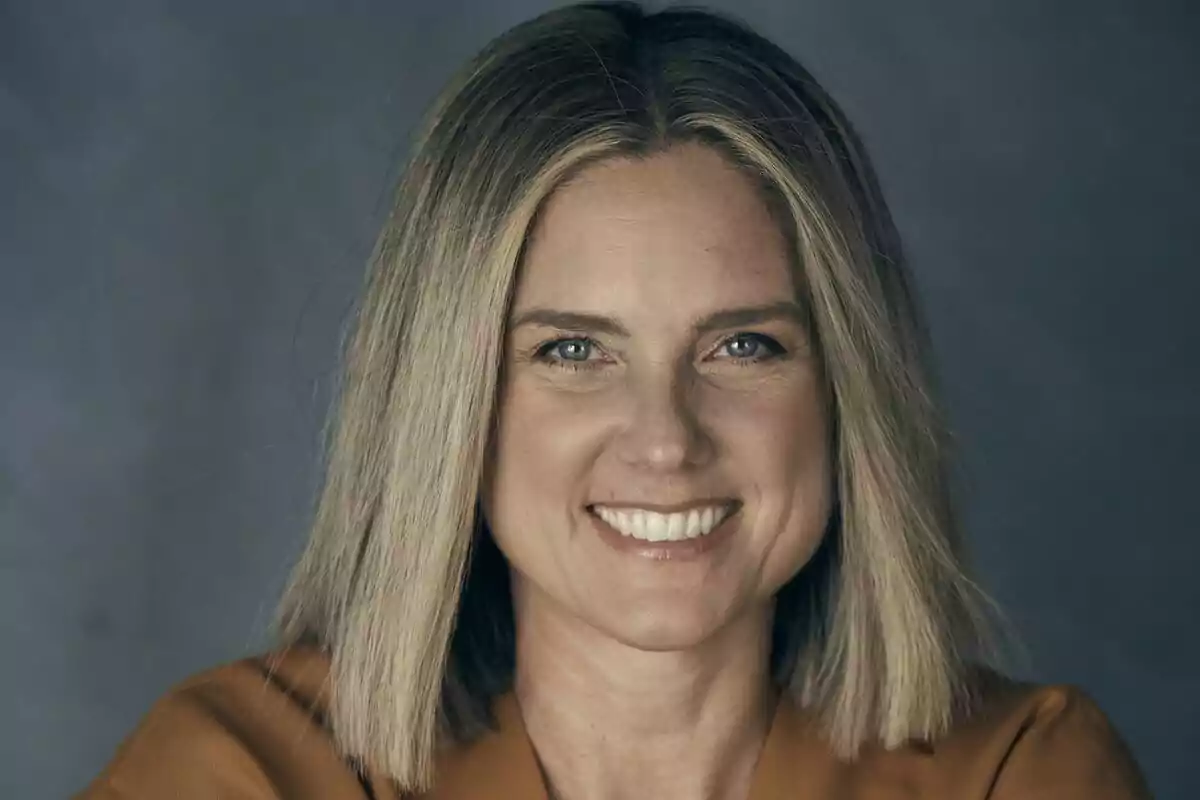 Fotografía de María José Rodríguez sonriendo con cabello rubio y lacio, fondo gris