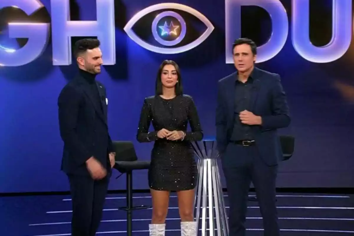 Suso Álvarez, Marieta Díaz y Ion Aramendi de pie en un set de televisión con un fondo que tiene un logotipo de ojo y letras grandes de GH DÚO.