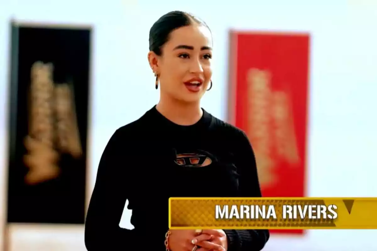 Marina Rivers de cabell fosc recollit i samarreta negra parlant davant de dos quadres desenfocats amb un requadre groc que mostra el nom Marina Rivers a 'Warrior Games'.