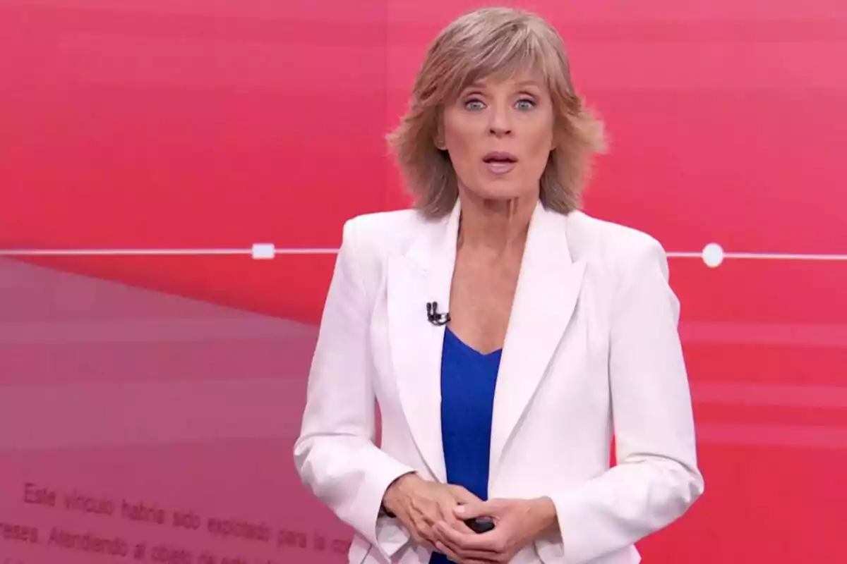 Marta Carazo rossa amb jaqueta blanca i brusa blava presentant en un estudi amb fons vermell