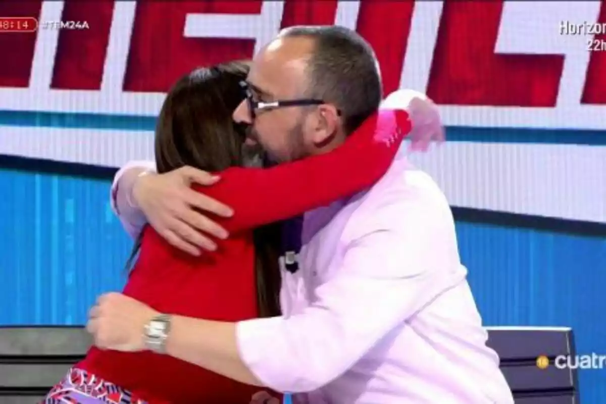 Marta Flich i Risto Mejide s'abracen a Tot és Mentida amb un fons de lletres grans i acolorides. Marta Flich i Risto Mejide s'abracen a Tot és Mentida amb un fons de lletres grans i acolorides.