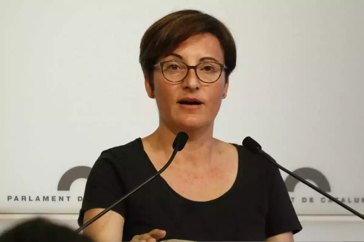 Woman with glasses speaking at a podium with microphones.