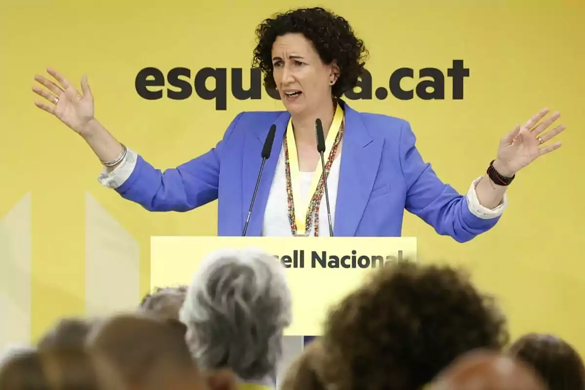 Marta Rovira amb jaqueta blava i samarreta blanca gesticula amb les mans aixecades mentre parla en un podi groc amb la inscripció "Consell Nacional" davant d'un fons groc amb el text "esquerra.cat".