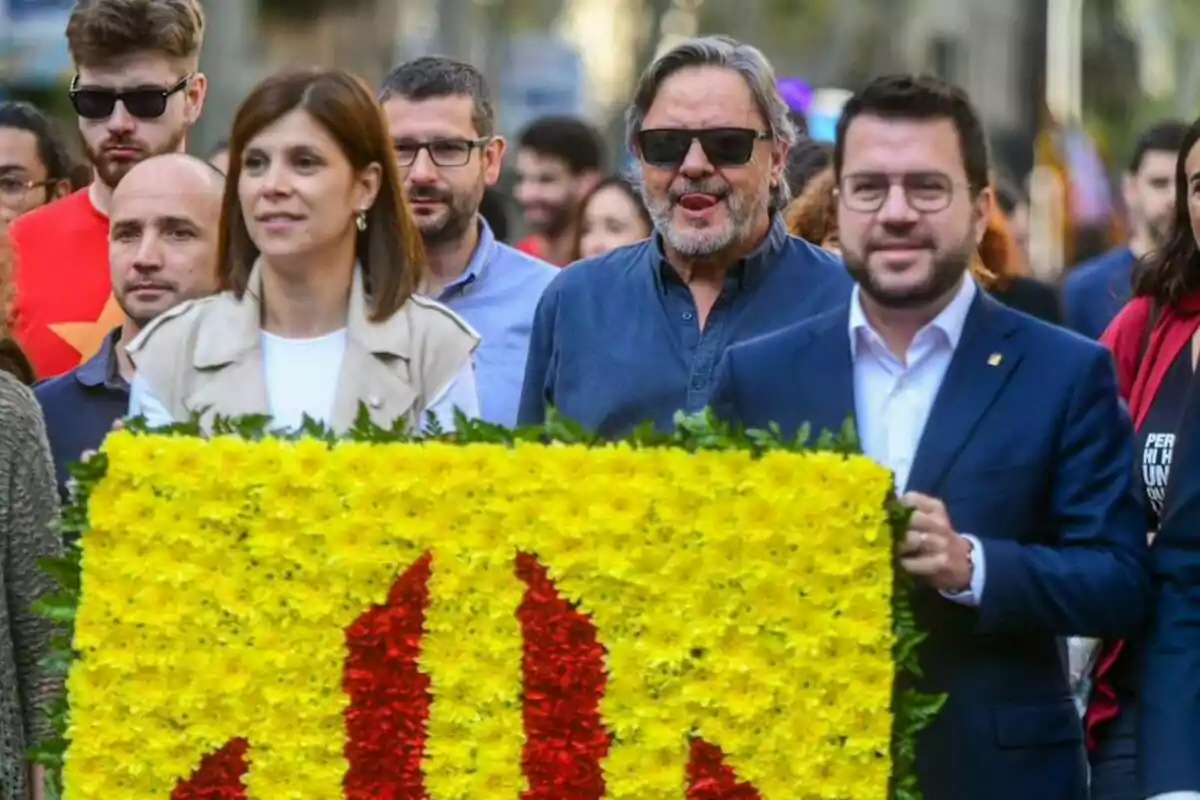 Un grup de persones participa en una manifestació, portant un arranjament floral amb els colors groc i vermell.