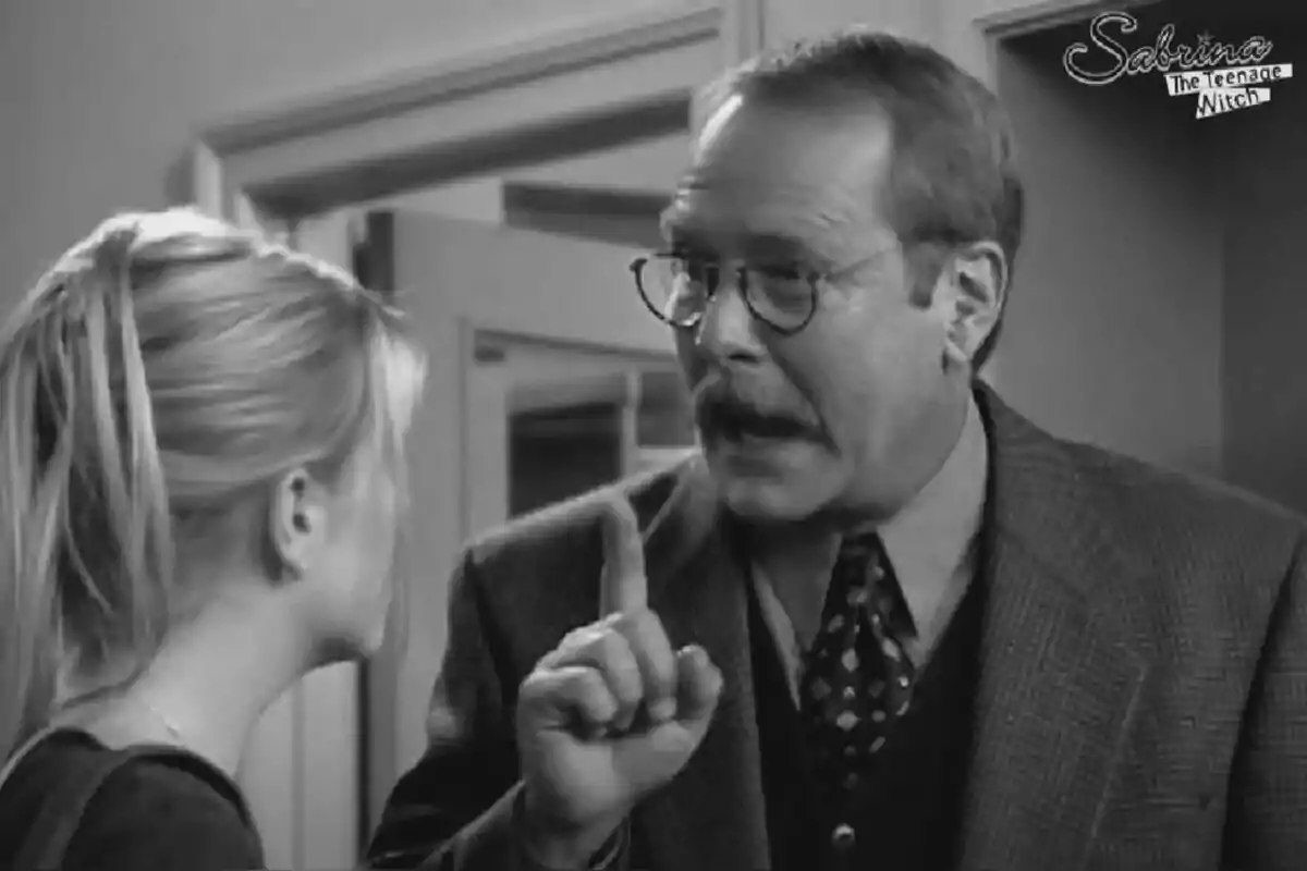 Fotografía de Martin Mull en una escena en blanco y negro de la serie "Sabrina, the Teenage Witch" donde un hombre con gafas y bigote está hablando con una joven rubia.