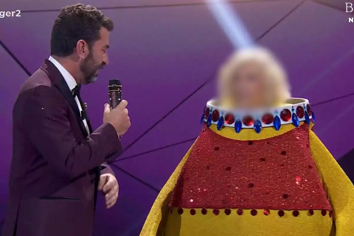 Arturo Valls amb micròfon parla amb una persona disfressada d'aneguet de goma amb la cara difuminada a Mask Singer.