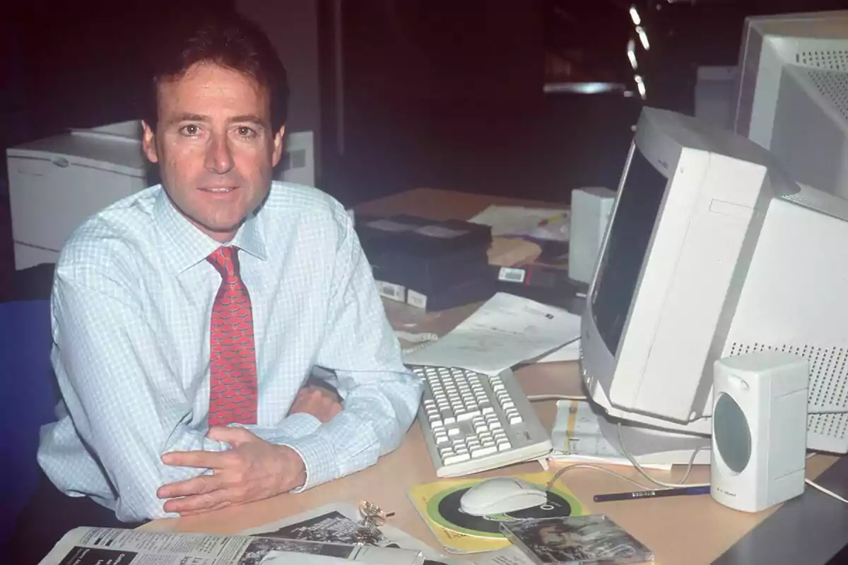Matías Prats amb camisa blanca i corbata vermella està assegut en un escriptori amb un ordinador antic, teclat, ratolí i diversos papers a Antena 3 Notícies. Matías Prats amb camisa blanca i corbata vermella està assegut en un escriptori amb un ordinador antic, teclat, ratolí i diversos papers a Antena 3 Notícies.