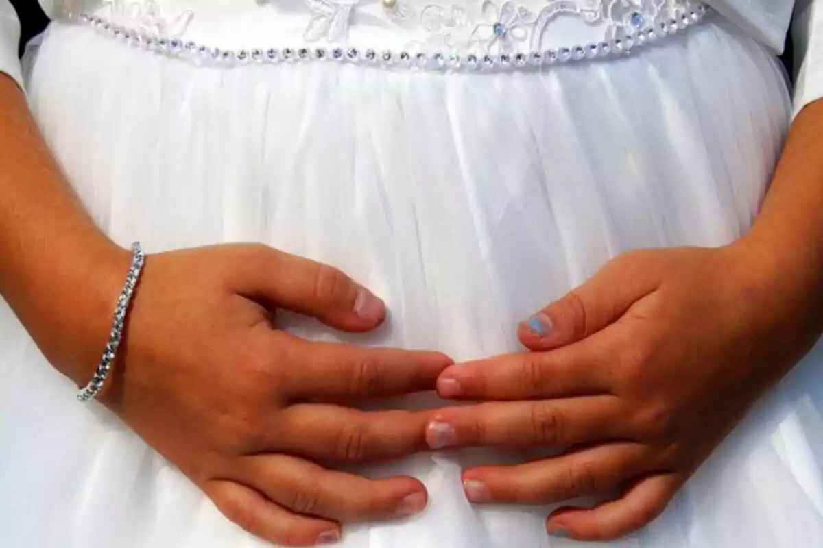 Young person's hands resting on a white dress with lace and pearl details.