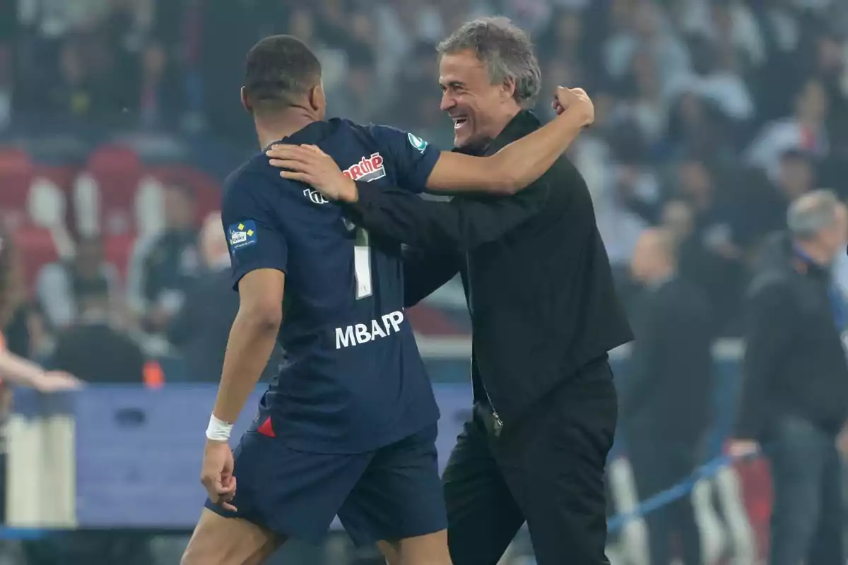 A soccer player and a coach hug each other on the playing field.