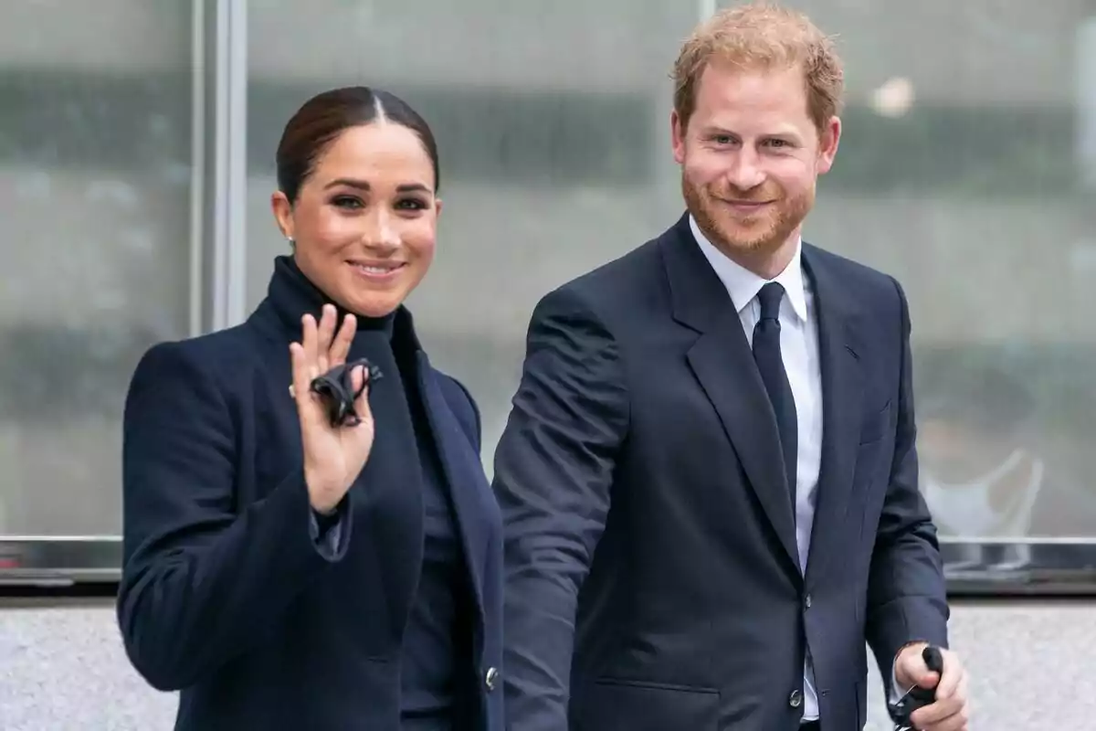 Meghan Markle and Prince Harry dressed formally, both smiling and walking together, she is waving.