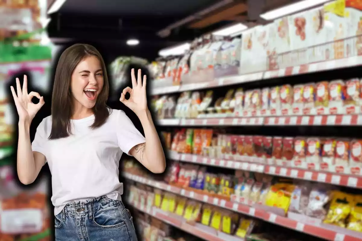 Noia bruna samarreta blanca i texans, picada d'ullet i fent el signe d'ok amb les dues mans, sobre fons de supermercat desenfocat