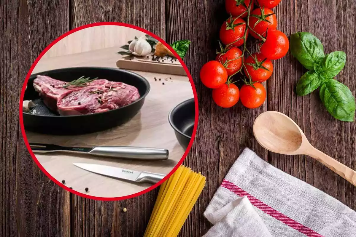 Detall taulell amb paella amb carn, ganivets i altres aliments i utensilis, sobre fons de taula de fusta amb tomàquets, alfàbrega, espaguetis crus, un drap i una cullera de fusta