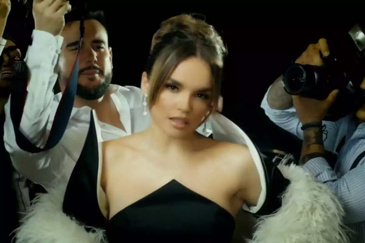 Melody con un elegante vestido negro y un abrigo de plumas blancas es fotografiada por varios fotógrafos en un ambiente de alfombra roja en el videoclip de Esa Diva.