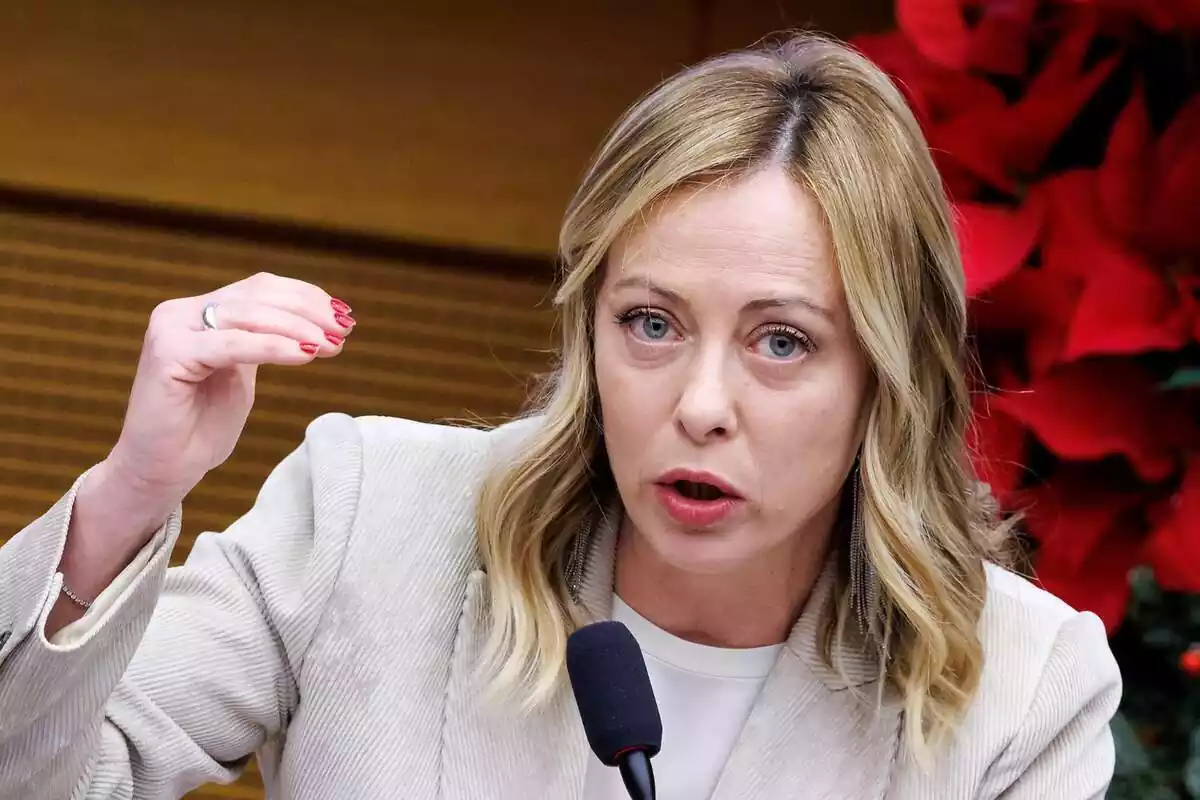 Medium close-up shot of Giorgia Meloni speaking and raising her right hand while looking at the camera