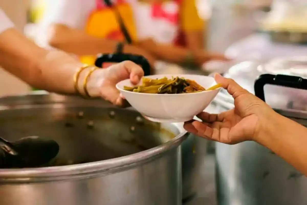 Una persona entrega un plato de comida a otra en un entorno de cocina comunitaria.