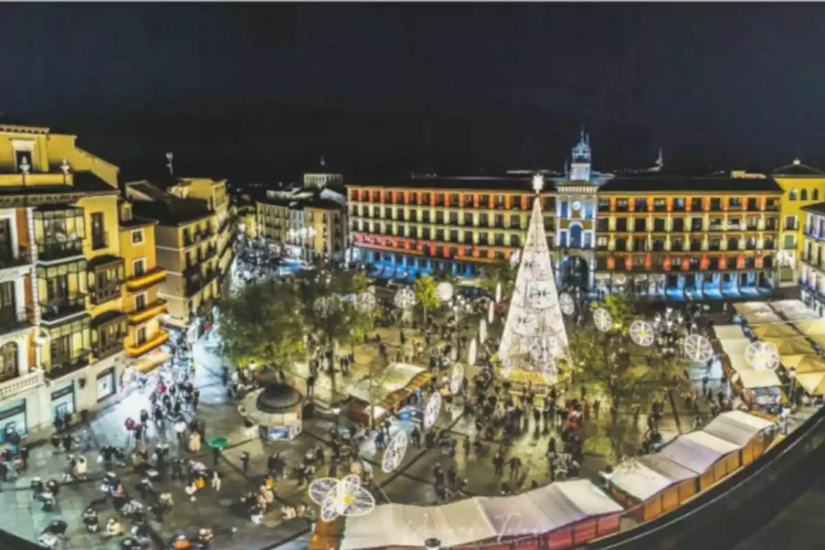 Vista nocturna d´una plaça il·luminada amb un arbre de Nadal i edificis al voltant.