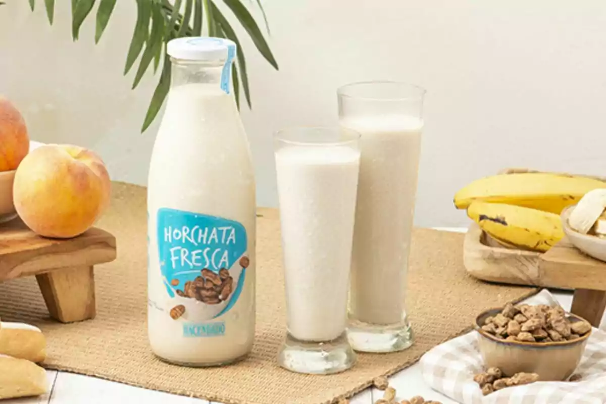Una ampolla d'orxata fresca al costat de dos gots plens de la beguda envoltats de fruites com préssecs i plàtans sobre una taula. Una ampolla d'orxata fresca al costat de dos gots plens de la beguda envoltats de fruites com préssecs i plàtans sobre una taula.