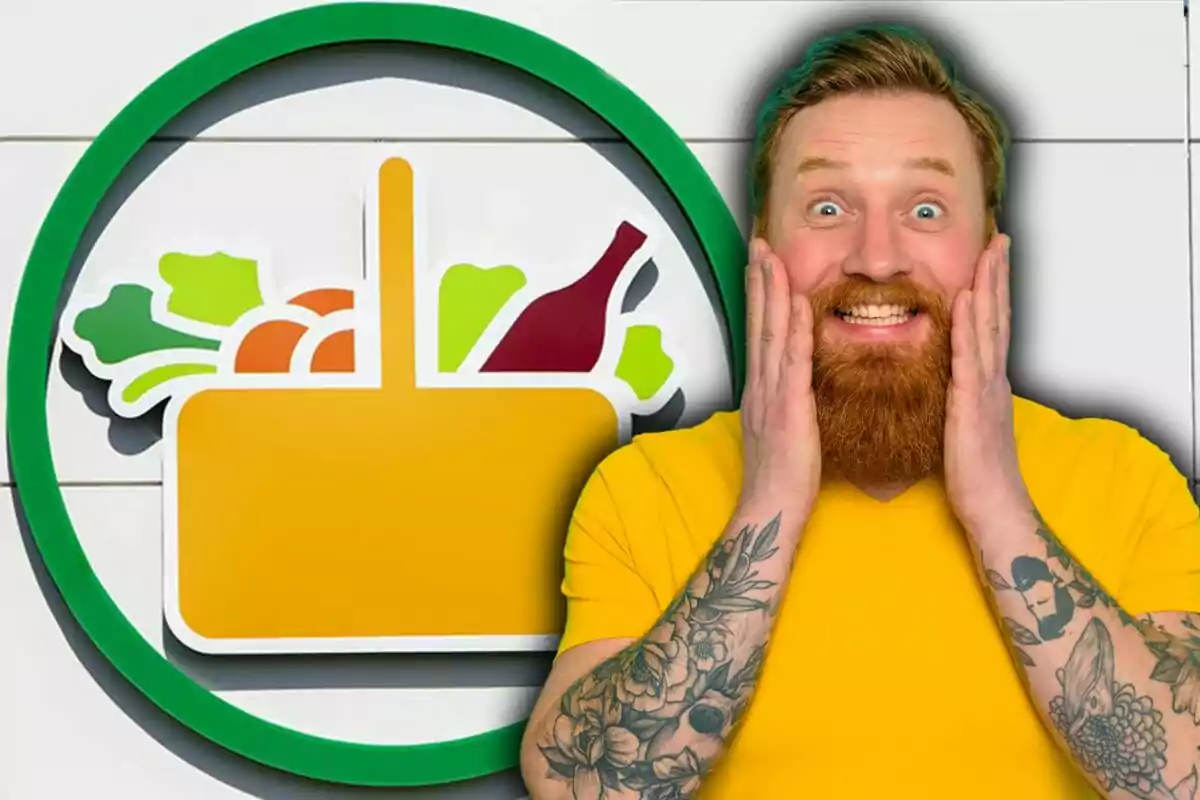 Home pèl-roig amb barba i samarreta groga somriu sorprès davant d’un logotip de supermercat amb verdures i una ampolla