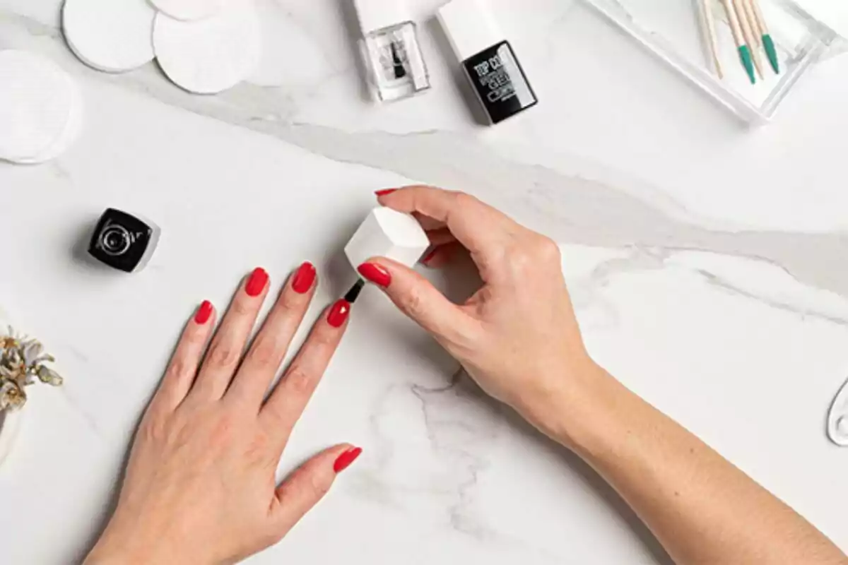 Manicure in progress with red nail polish on a marble table, surrounded by manicure tools. Manicure in progress with red nail polish on a marble table, surrounded by manicure tools.