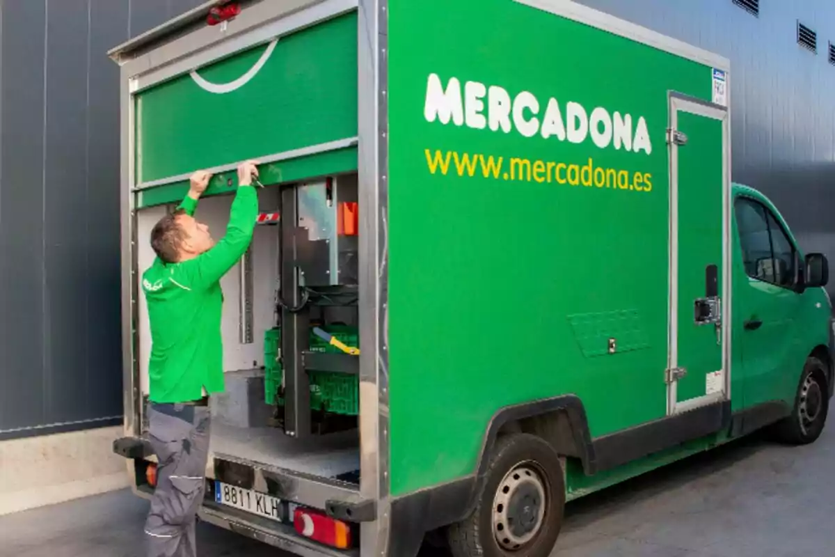 A man opens the back door of a green Mercadona truck parked next to a building.