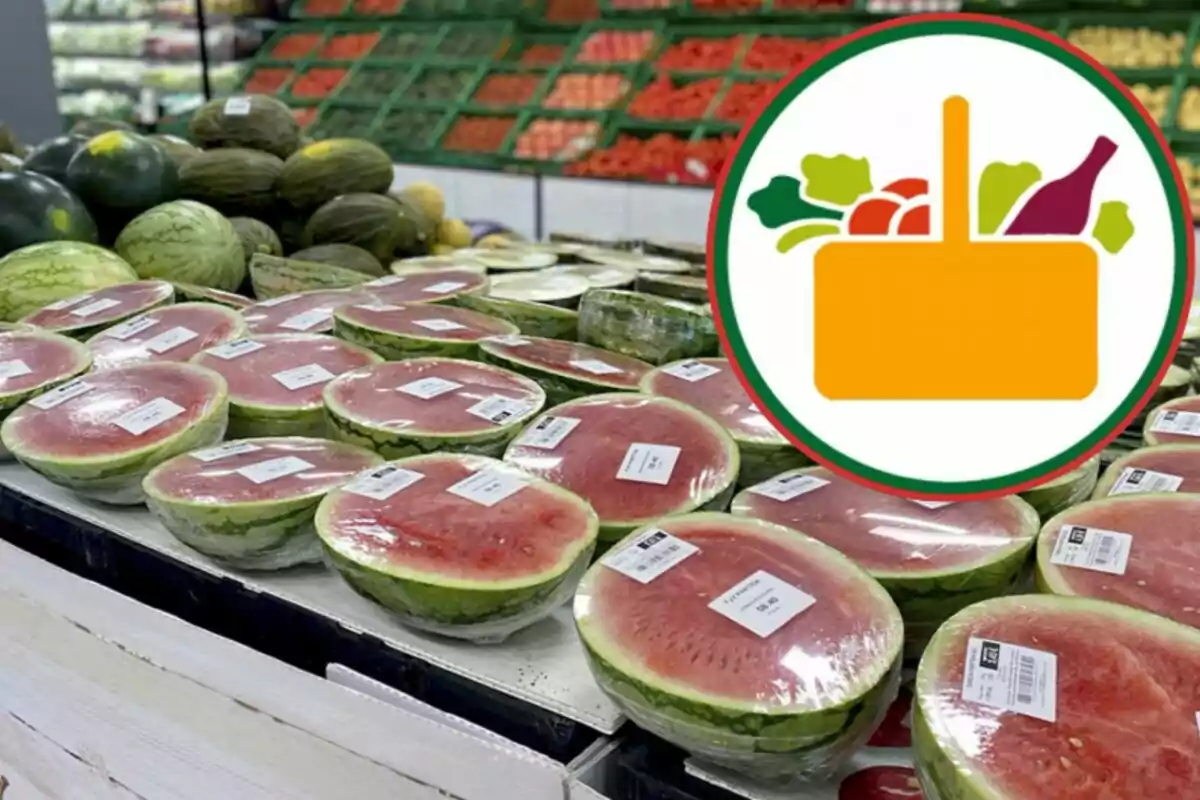 Una secció de fruites en un supermercat amb síndries tallades i embolicades amb plàstic, juntament amb un logotip d'una cistella de compres amb fruites i verdures.