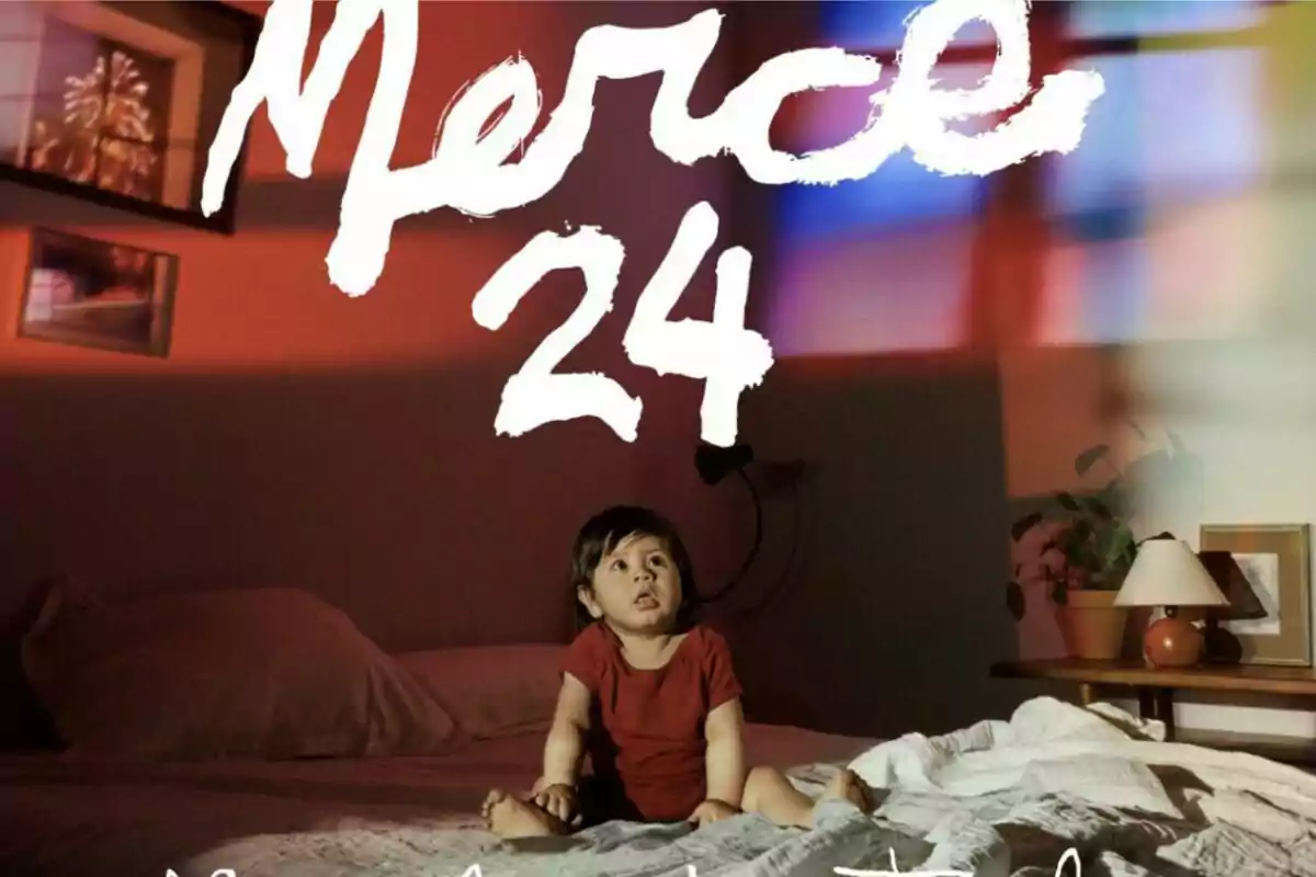 Un nen petit assegut en un llit amb la paraula "Merce 24" escrita d'allò més bé sobre ell, en una habitació il·luminada amb llums de colors.