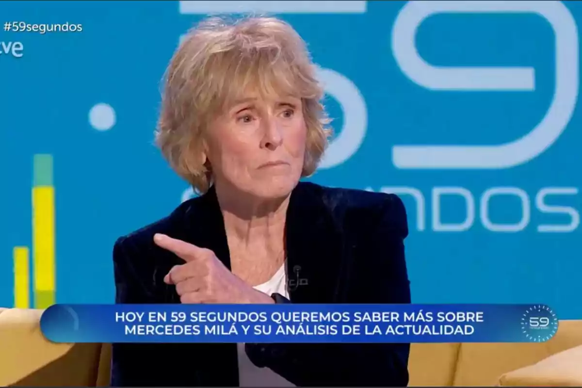 Mercedes Mila con cabello rubio está sentada en un programa de televisión llamado "59 segundos" con un fondo azul y un texto en la pantalla que menciona un análisis de la actualidad.