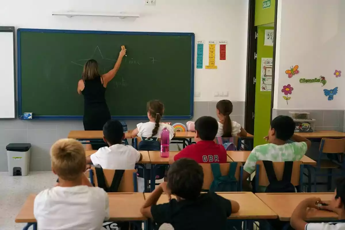 Una mestra escriu a la pissarra mentre els estudiants l'observen en un saló de classes.