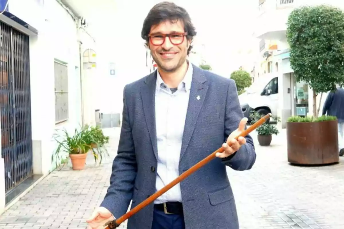 A man with red glasses and a blue suit holds a cane on a pedestrian street. A man with red glasses and a blue suit holds a cane on a pedestrian street.