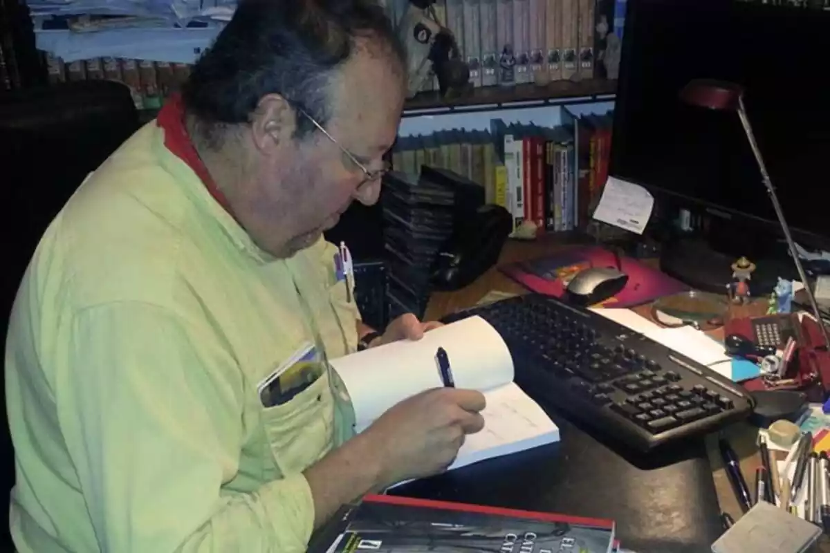 Fotografia de perfil de Miguel Aracil assegut al seu escriptori signant un dels seus llibres
