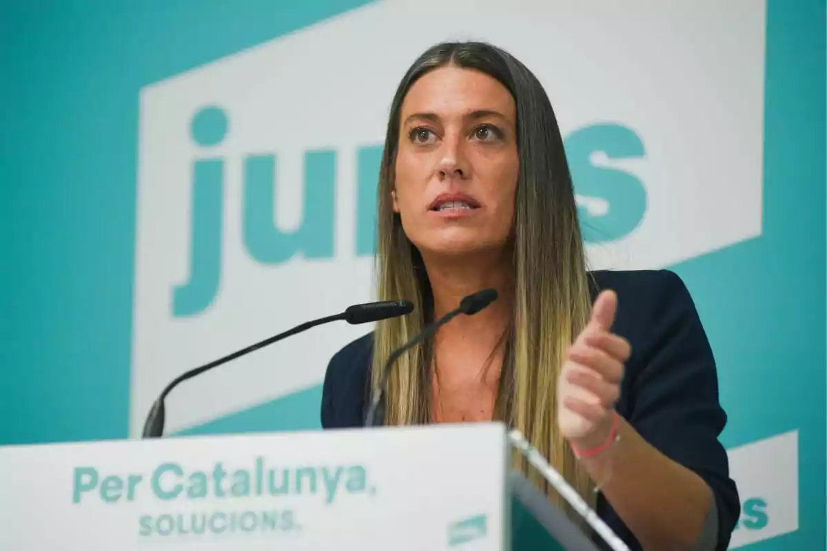 Mujer hablando en un podio con fondo verde y texto de campaña política.