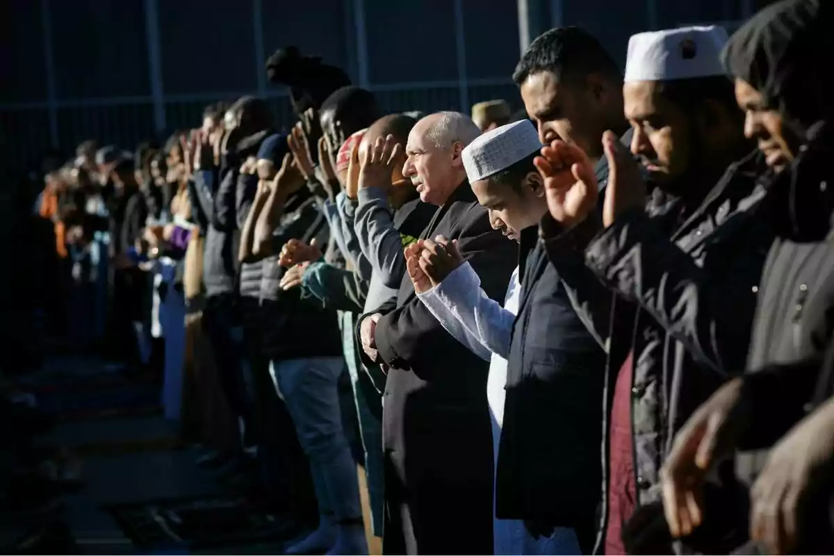 A group of people lined up participating in an outdoor prayer, with their hands raised and eyes closed.