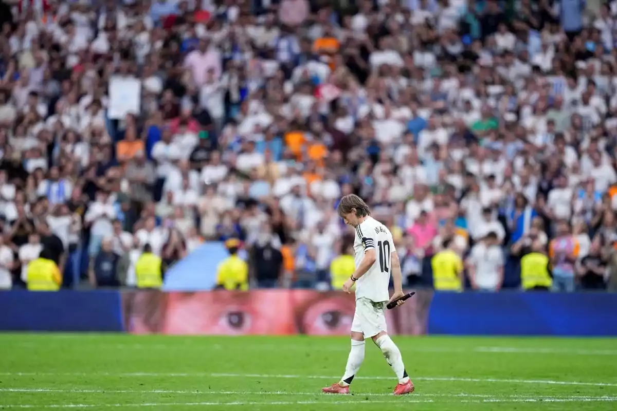 Soccer player wearing number 10 and the captain's armband walks with his head down across the field while the crowd watches from the stands. Soccer player wearing number 10 and the captain's armband walks with his head down across the field while the crowd watches from the stands.