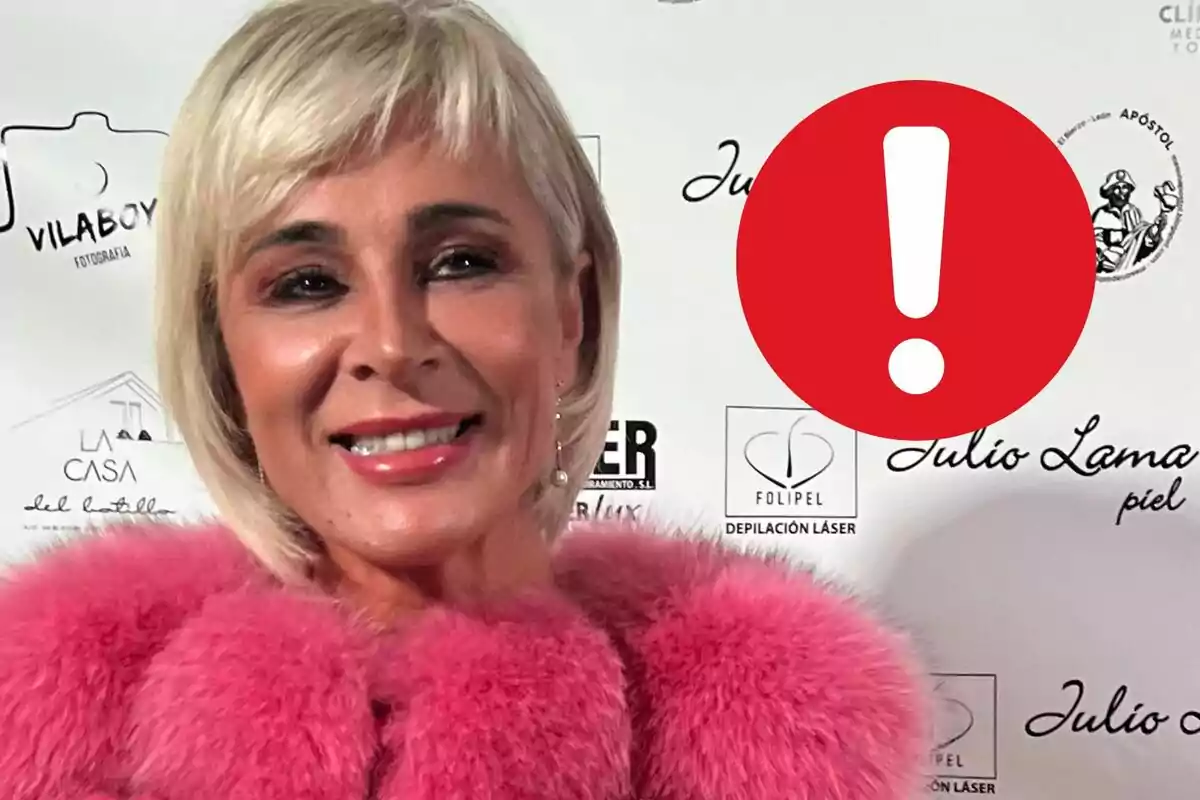 Ana María Aldón con cabello rubio y abrigo rosa posando frente a un fondo con logotipos y un icono de advertencia en rojo.