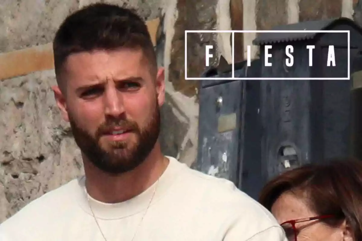 David Rodríguez con barba y cabello corto está de pie frente a una pared de piedra, al lado de una persona con gafas rojas, con la palabra "FIESTA" en la parte superior derecha.